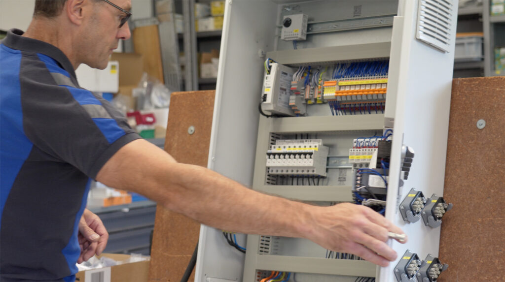 Mitarbeiter der Elektro Kaufmann GmbH, der vor einem offenen Schaltschrank mit diversen elektronischen Bauteilen arbeitet.