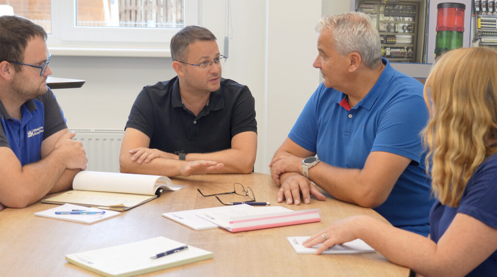 Mitarbeiter und Mitarbeiterinnen der Elektro Kaufmann GmbH, sitzen an einem Tisch und haben ein Meeting.