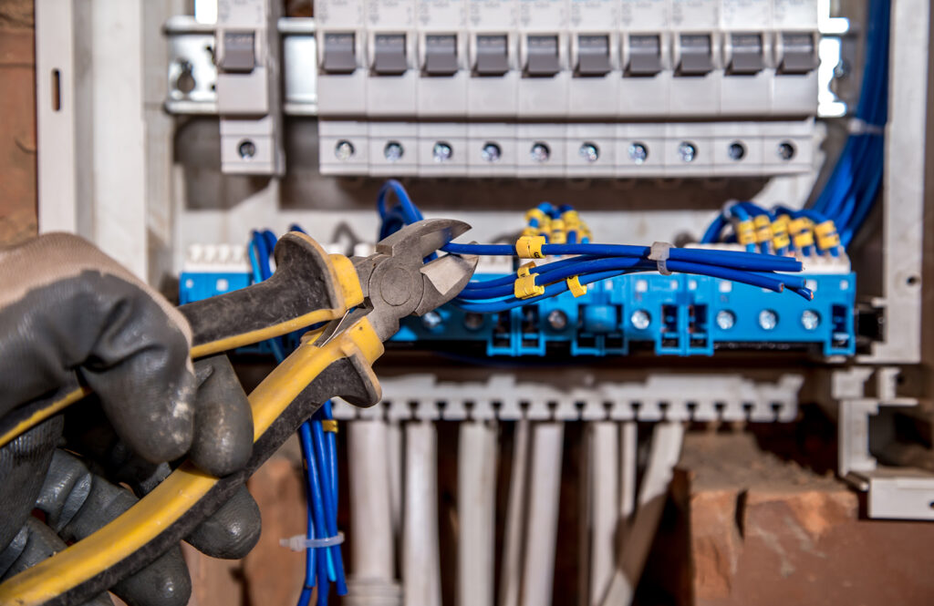 Ein Mitarbeiter der Elektro Kaufmann GmbH trennt ein Kabel an einem offenen Schaltschrank.