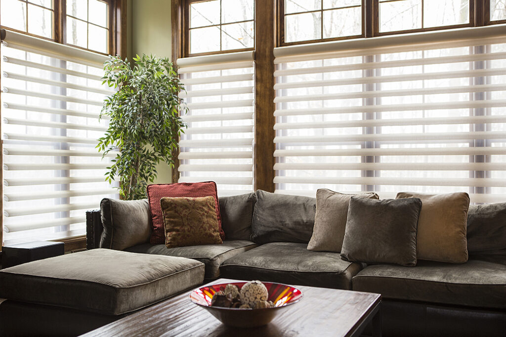 Gemütliche Couch in einem Wohnzimmer, vor einer Fensterfront mit Sonnenschutz.